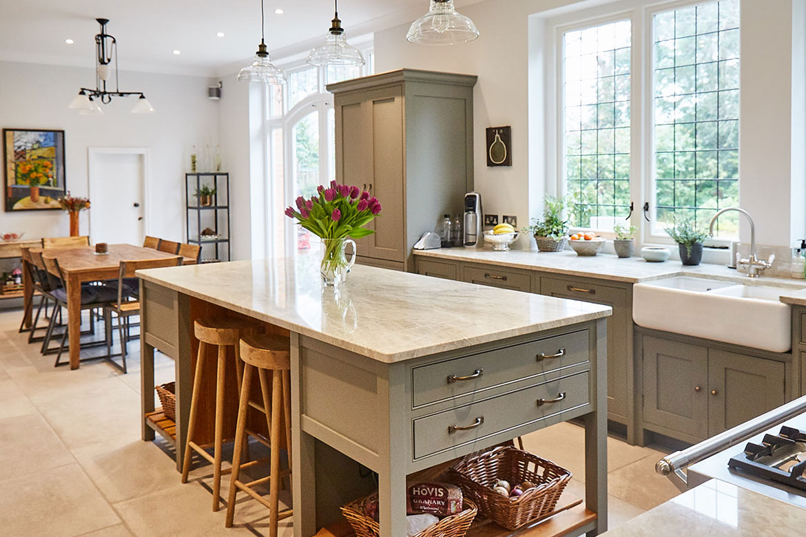 Oak breakfast bar stools sit under grey moss freestanding kitchen island with flowers on worktop