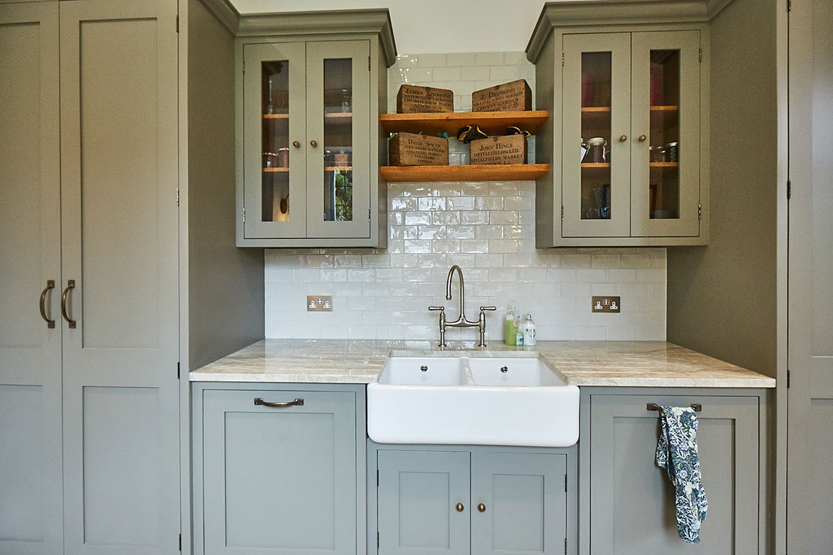 Belfast Sink unit against white metro tiles, glass wall cabinets, and open solid oak shelves