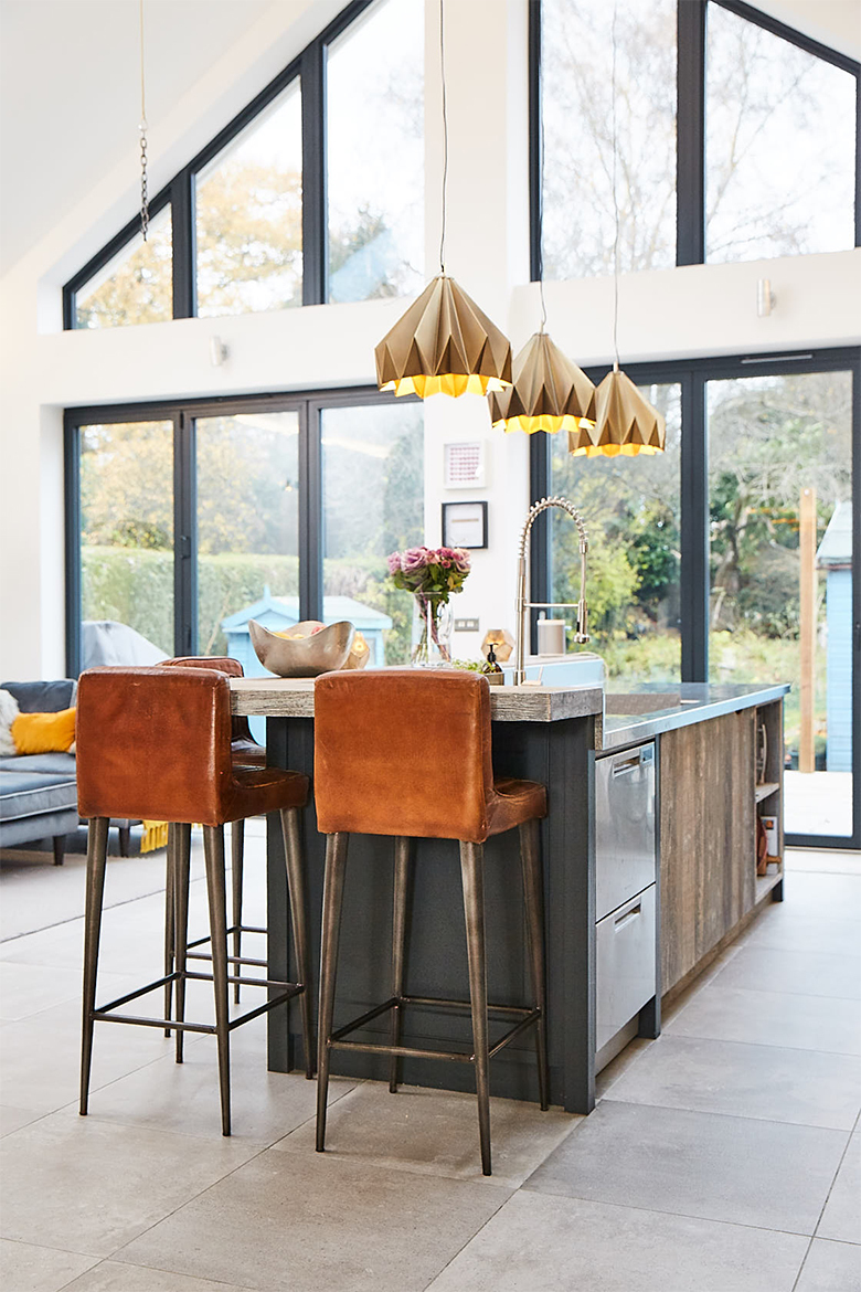 Large vaulted room with huge glass windows and reclaimed rustic painted kitchen island and brown leather chairs
