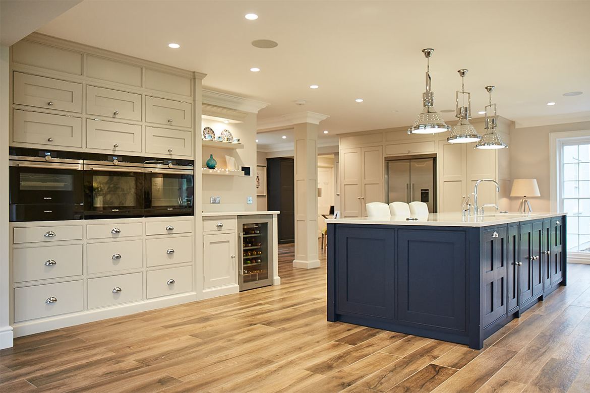 Eye level ovens in bespoke painted light grey kitchen cabinets behind blue island