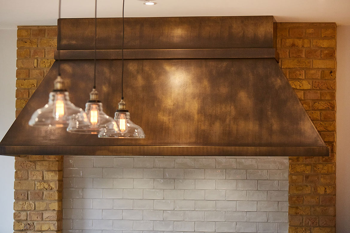 Glass pendant lights shine on aged brass bespoke canopy for extractor