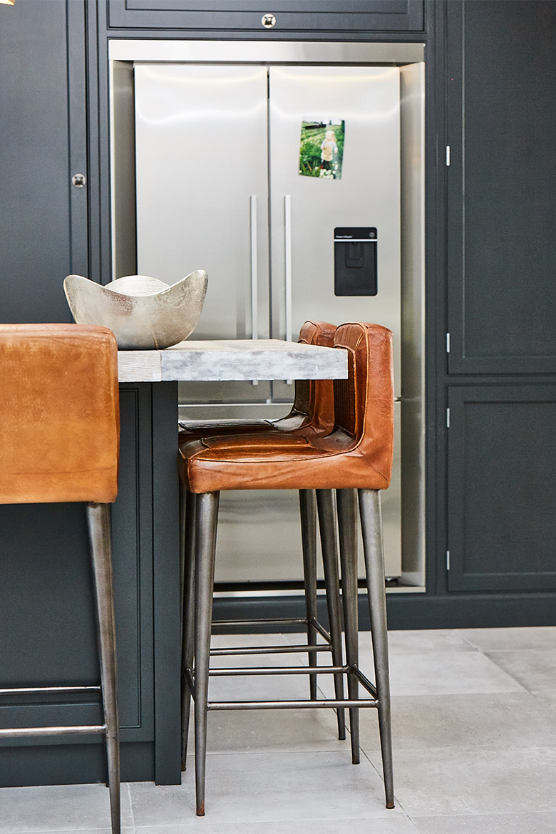 Leather and metal bar stool under bespoke kitchen island painted dark black with reclaimed worktop