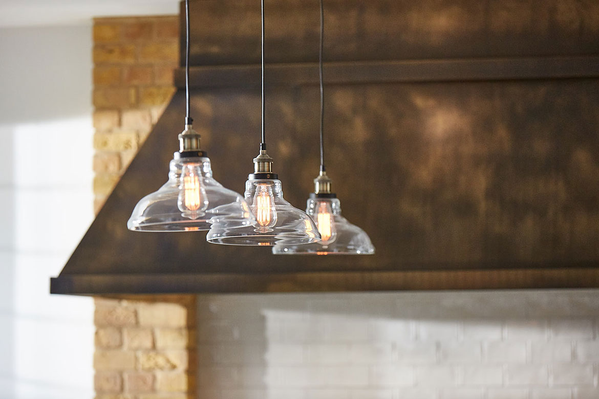 Three delicate glass pendant lights with aged brass canopy in background