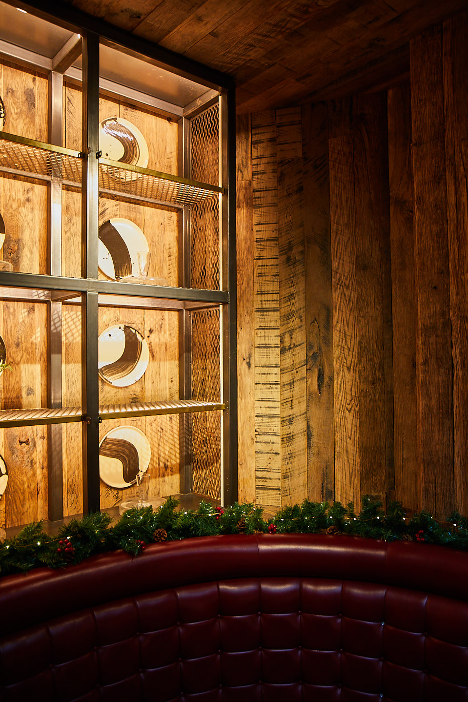 Red leather seating booth with industrial shelving with round mirrors behind hung on wood cladded wall