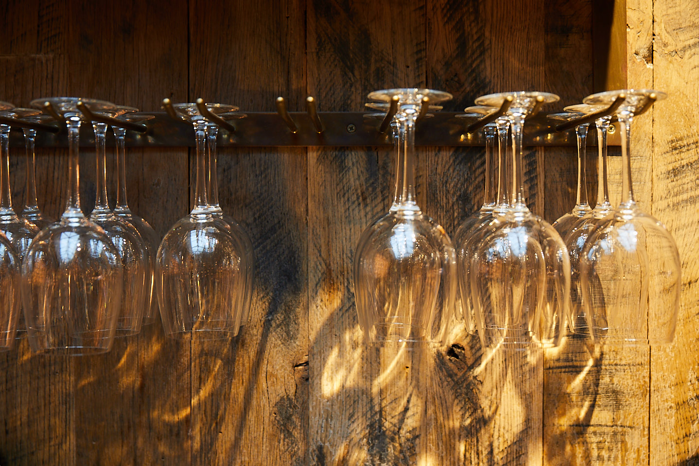 Wine glasses hang from metal rails with reclaimed clad wall