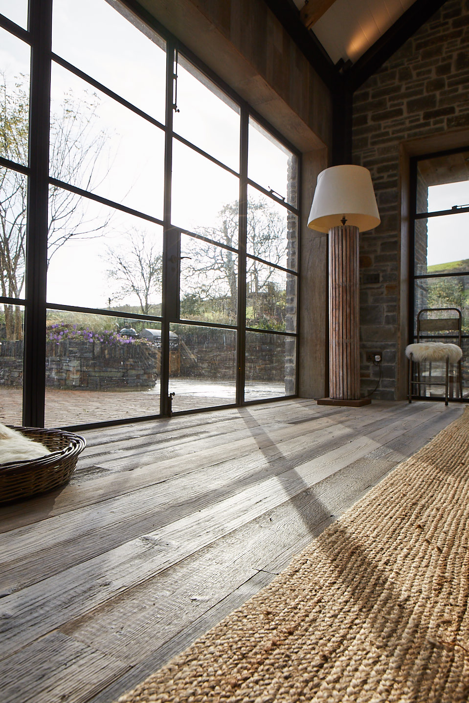 Shadow of crittall door shines across reclaimed wood floor boards and rustic rug