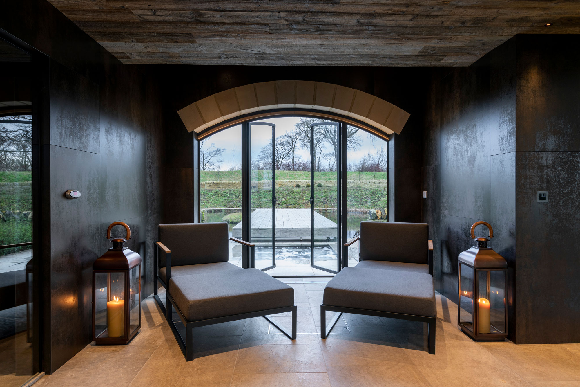 Two grey upholstered occasional chairs in front of large glass windows and cladded wood ceiling