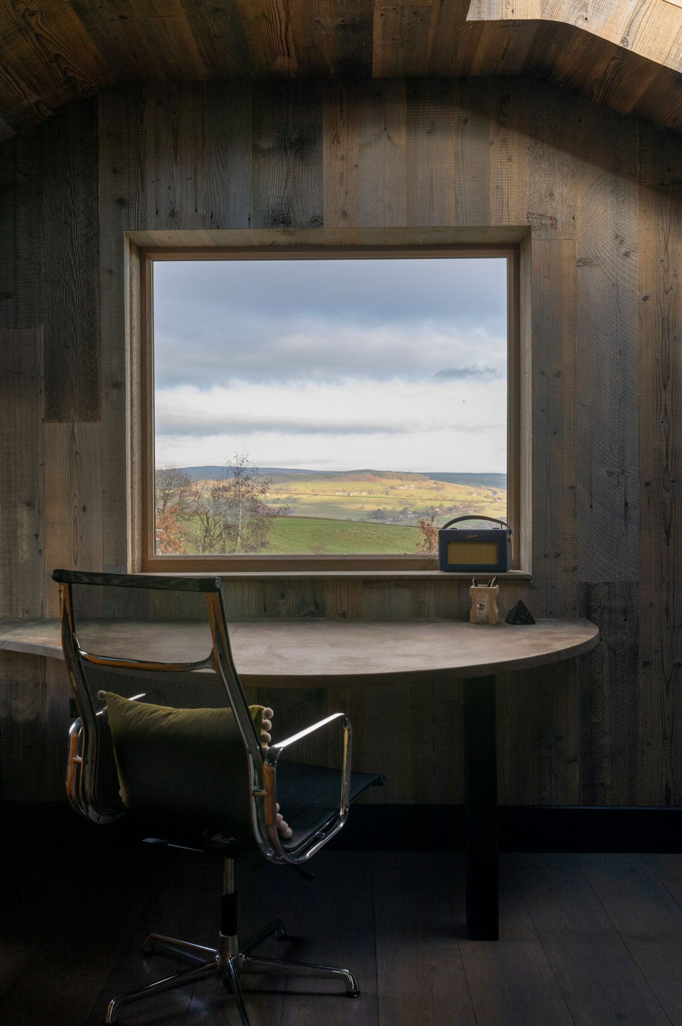 Office desk and chair in front of window in a fully cladded wood room