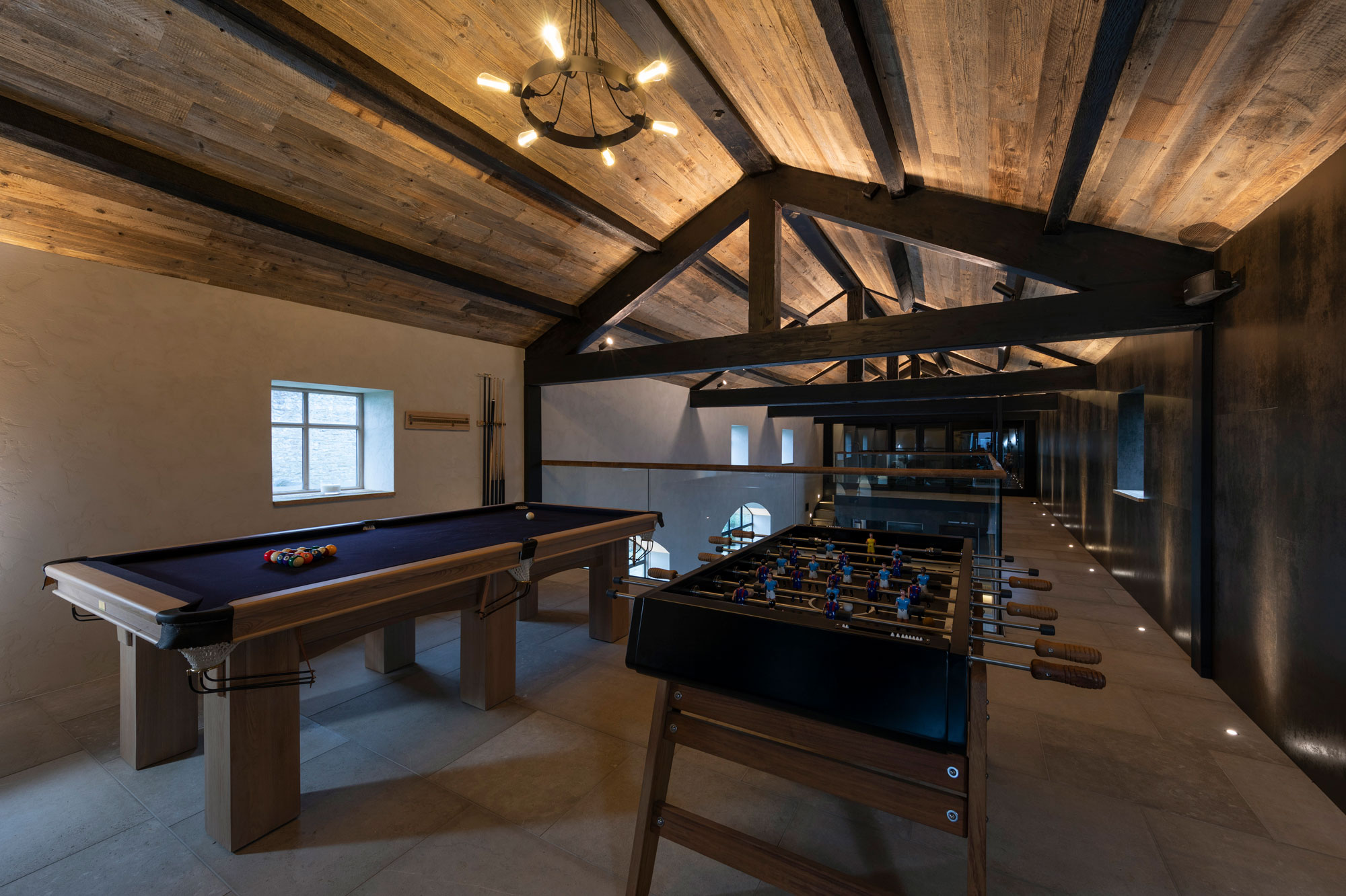 Pool table and foosball table in large room with tiled floor on wood clad ceiling