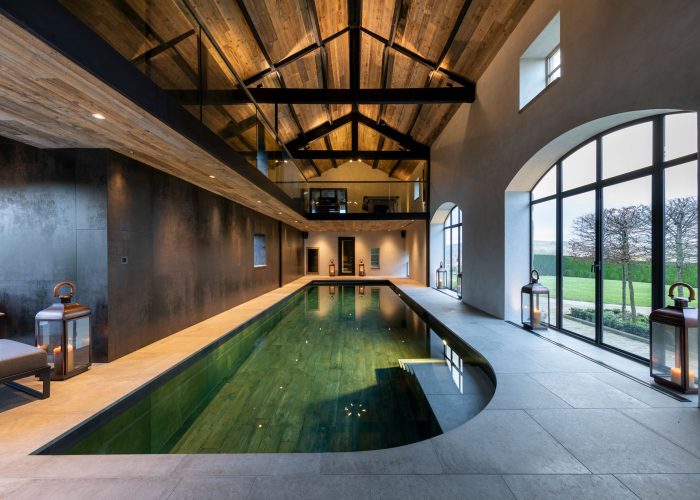 Balcony above indoor swimming pool shining lights on to cream tiled walkway