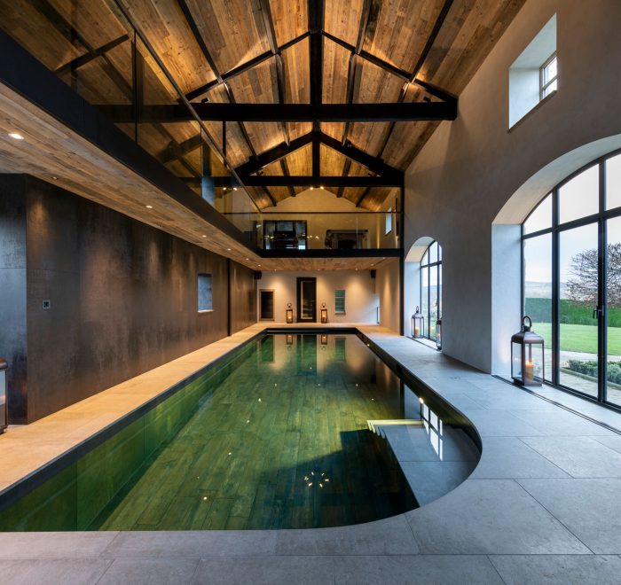 Balcony above indoor swimming pool shining lights on to cream tiled walkway