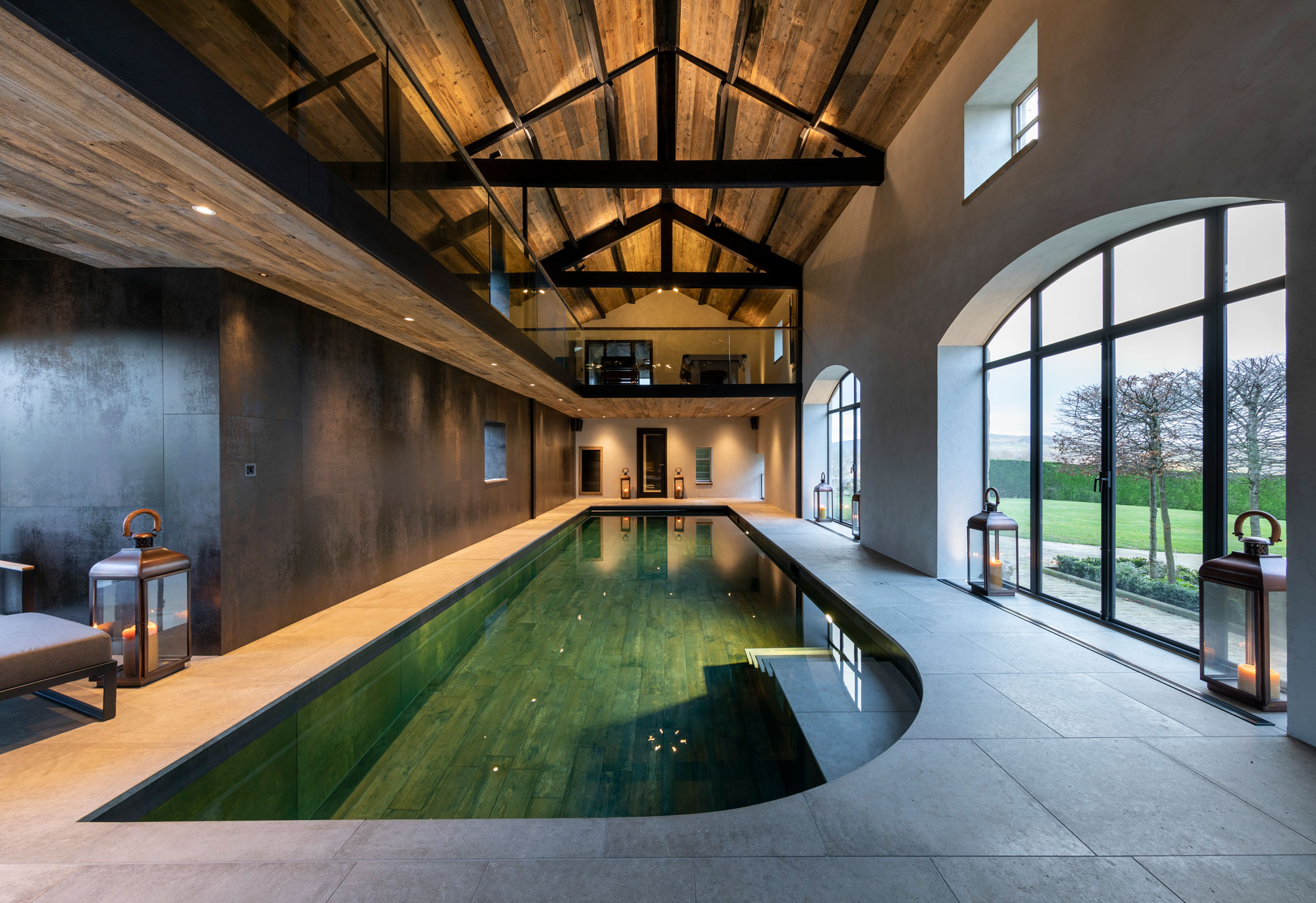 Balcony above indoor swimming pool shining lights on to cream tiled walkway