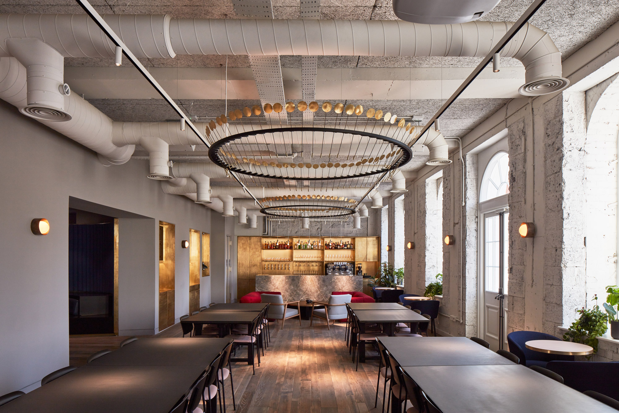 Large chandelier above dining tables and chairs with brass bar in background