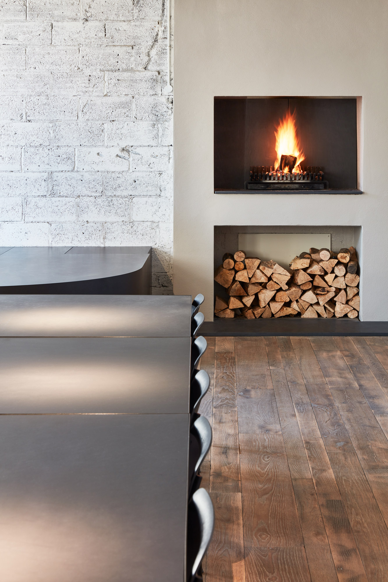 Black dining table with burning fire in background and log storage