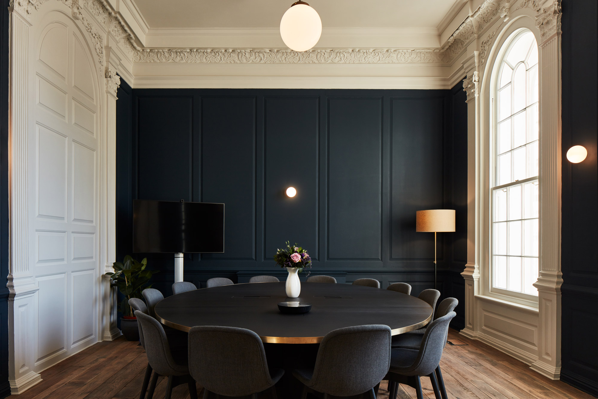 Round dining table with upholstered chairs and painted blue panelled wall