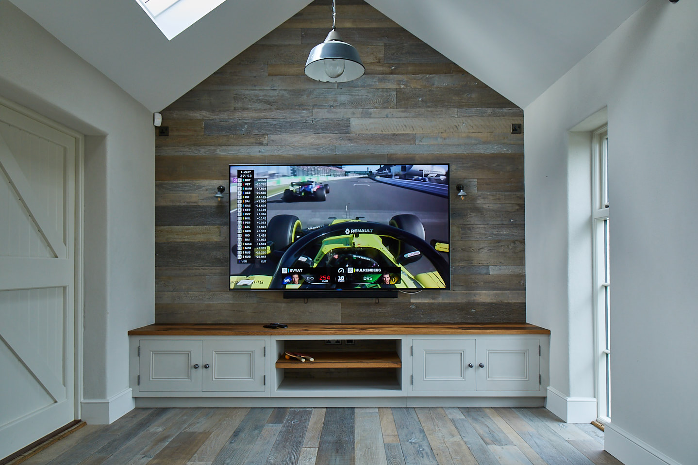 High vaulted room with oak cladded wall with tv mounted above low painted unit