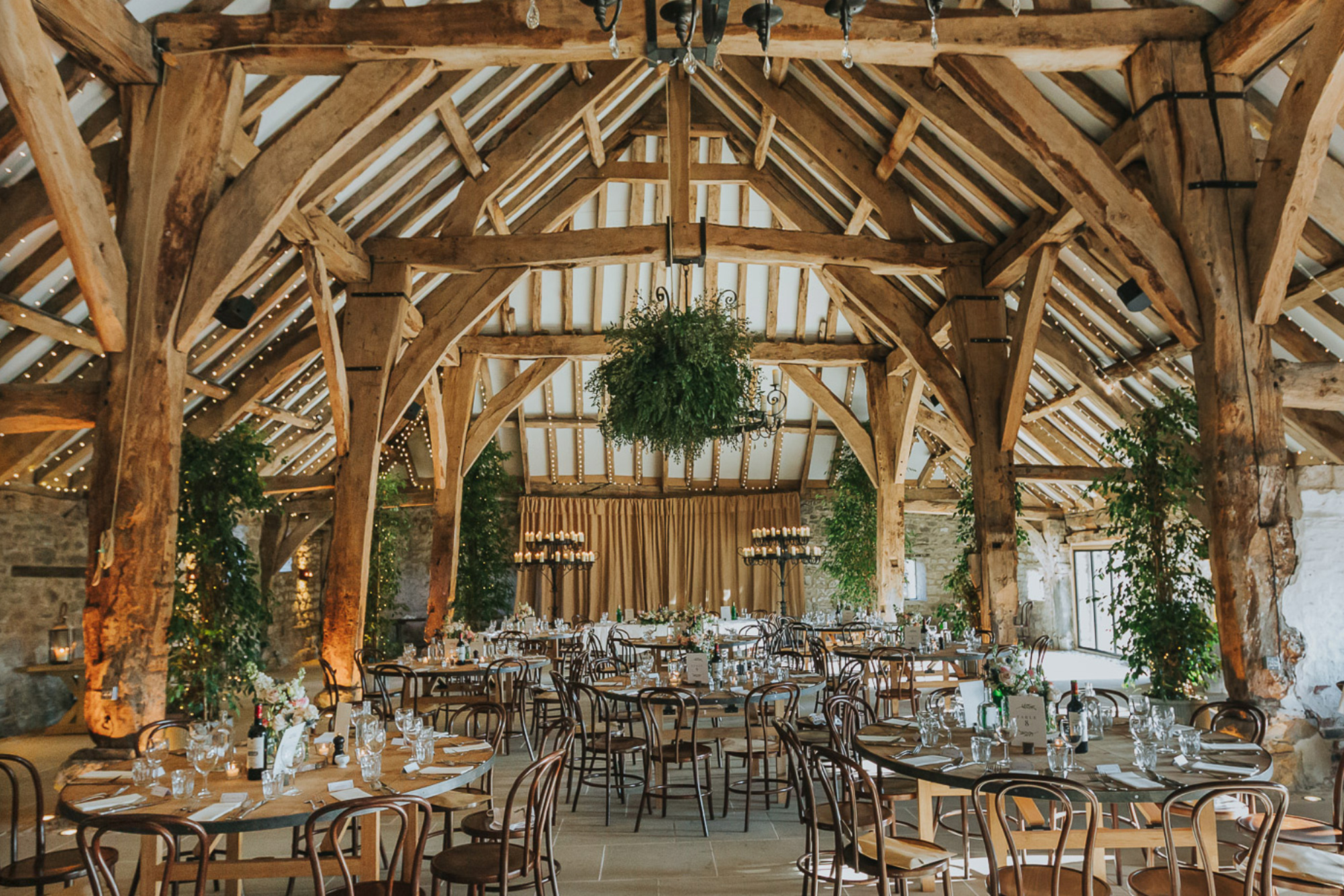 Round dining tables set for wedding reception in large oak beam farmhouse building