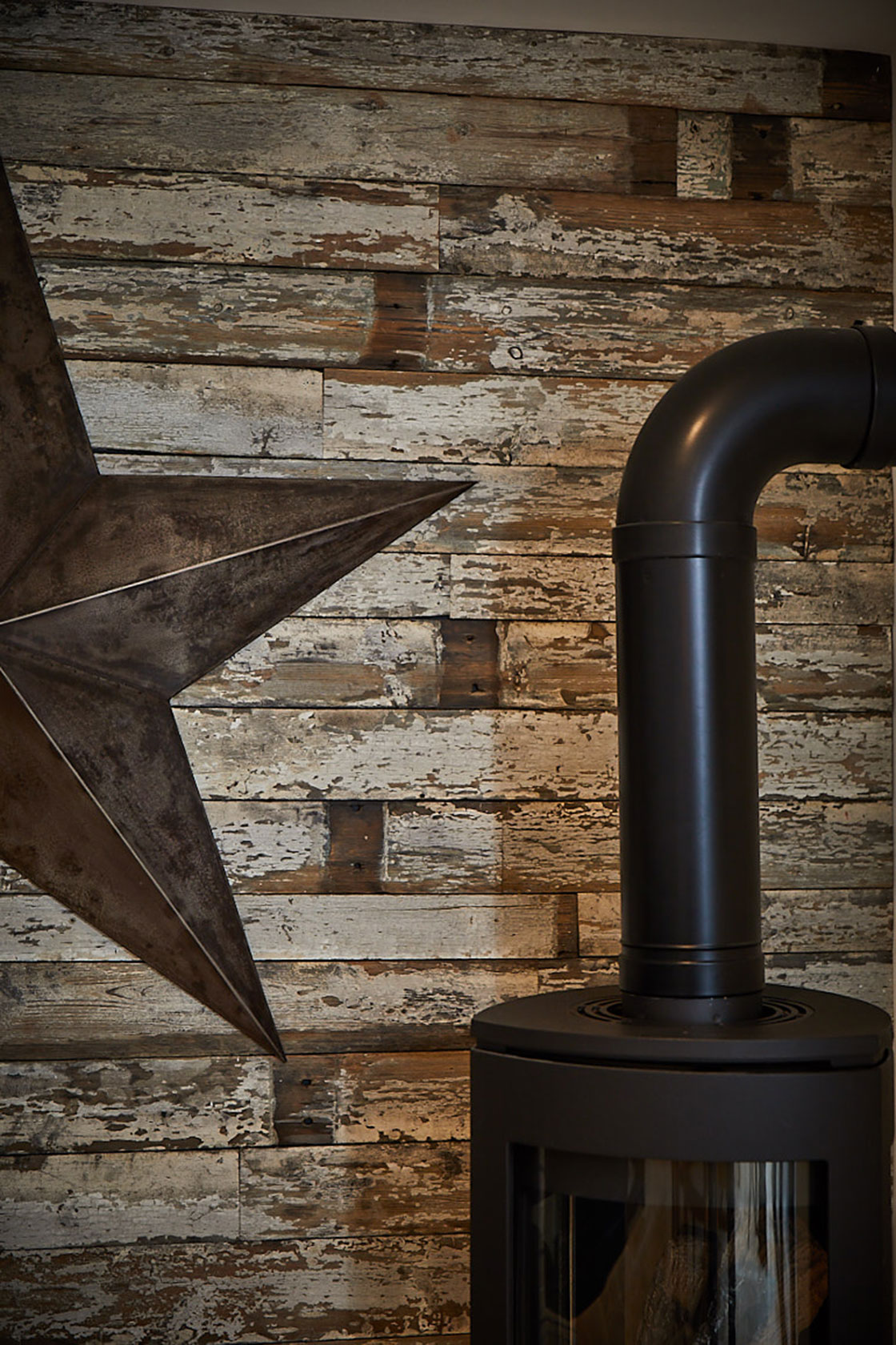 Black log burner with reclaimed rustic wall clad and large metal star