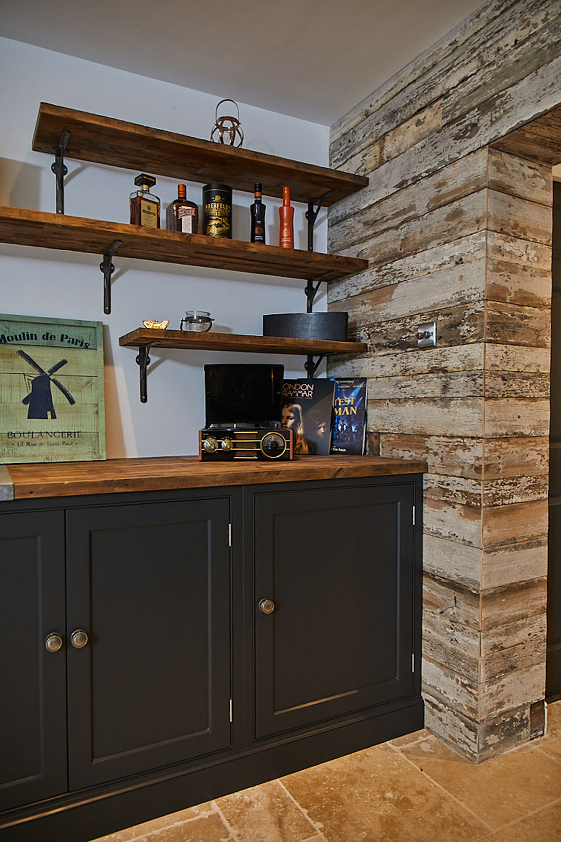 Dark blue bespoke painted units next to crackled white wall cladding and open rustic shelves with cast brackets