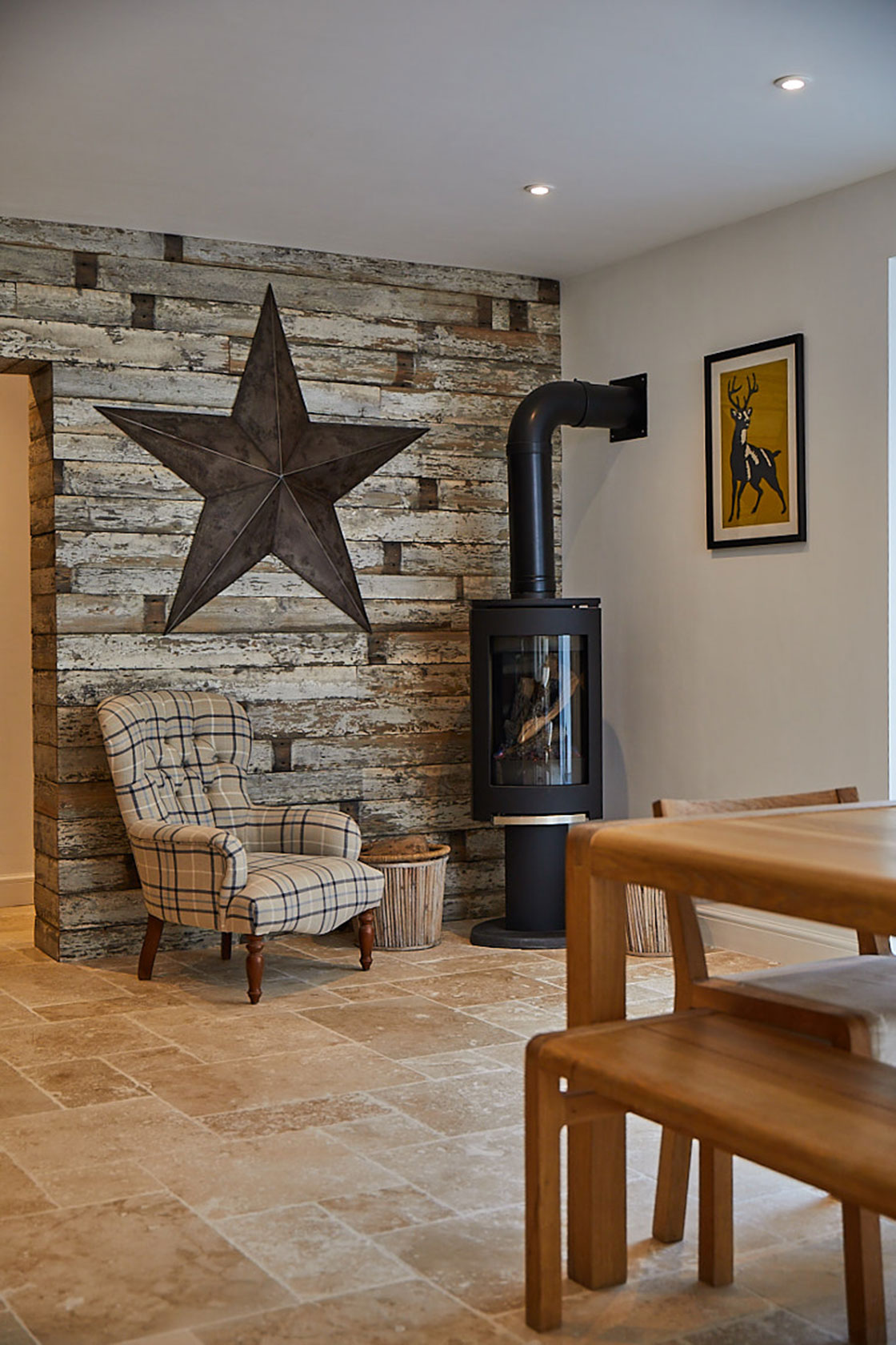 Upholstered occasional chair next to log burning fire and cladded wood wall