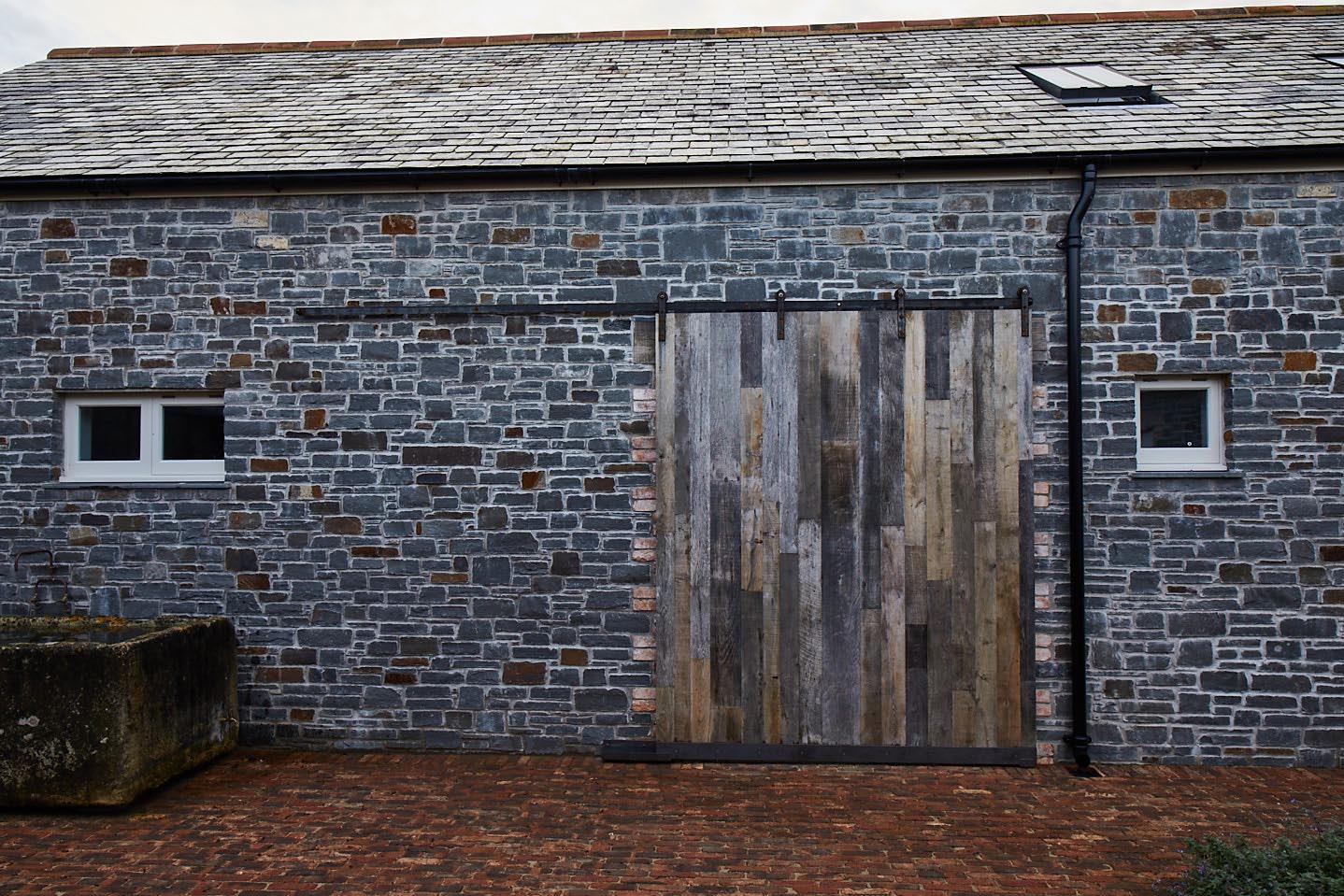 Closed external rustic pine sliding barn door against stone barn