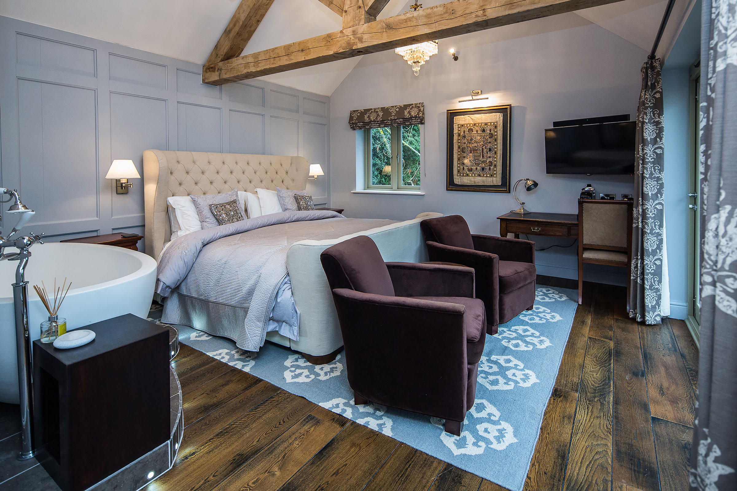 Cream bed with enginnered oak floor and upholstered purple chairs