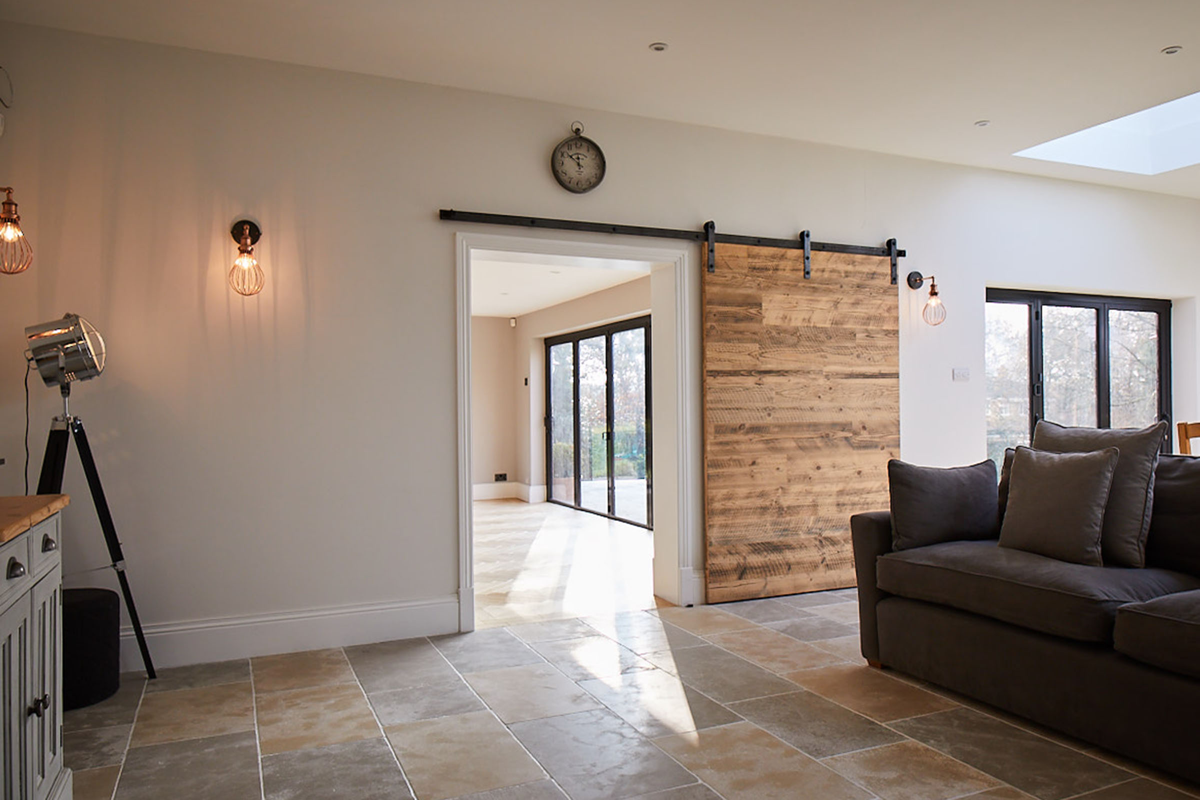 Internal sliding door with raw steel rail next to floor lamp and grey sofa