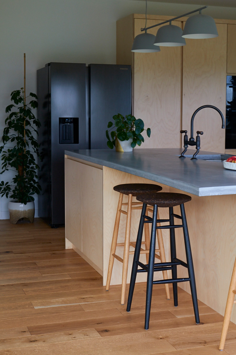 Kitchen island with plywood units and concrete worktop sit beside stainless steel fridge freezer