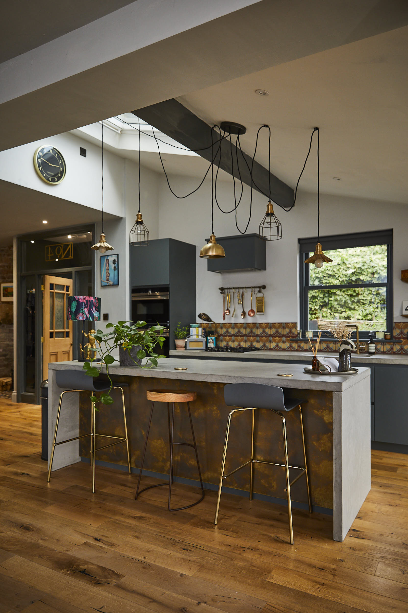 Bar stools sit under kitchen island with concrete waterfall worktop and clean oak flooring