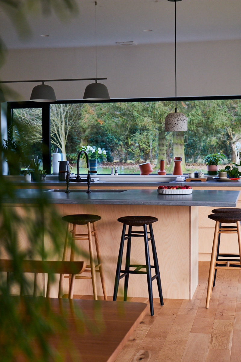 Stools sit under concrete breakfast bar in light birch wood kitchen