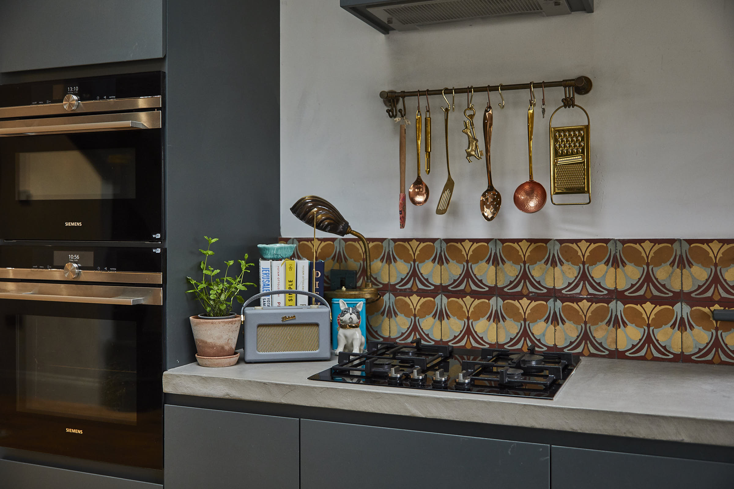 Copper utensils hand over gas hob with colourful shell tiles