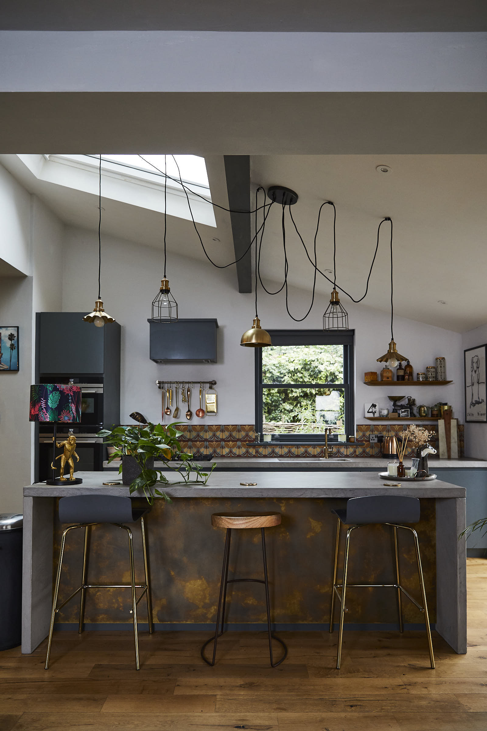 Stools under bespoke kitchen island made from concrete and brass with pendant lights hanging from above