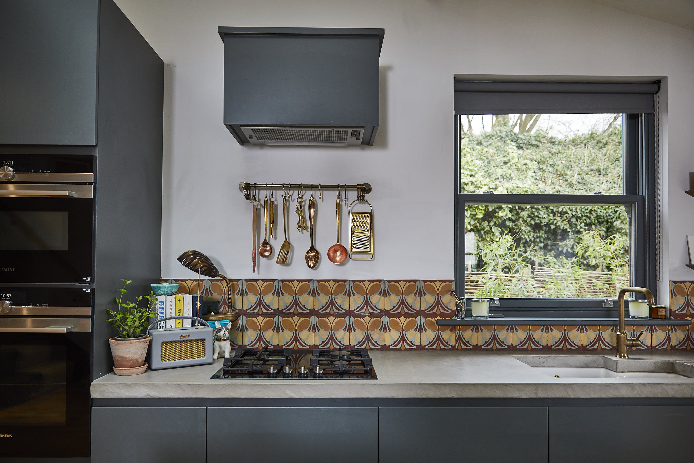Copper kitchen utensils sit under painted kitchen extractor with tiled backsplash