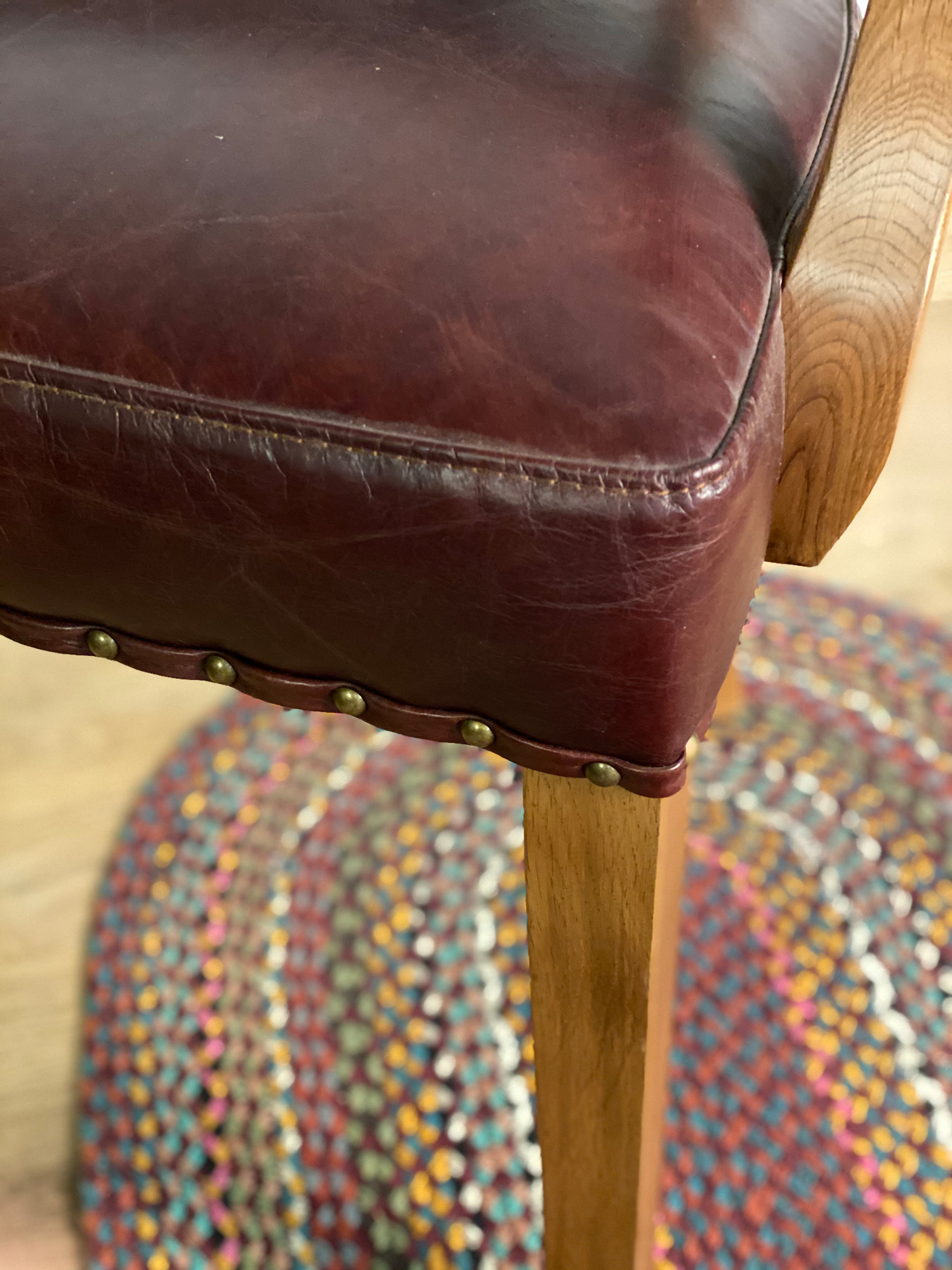 Red leather office chair seat detail with brass studs and oak legs