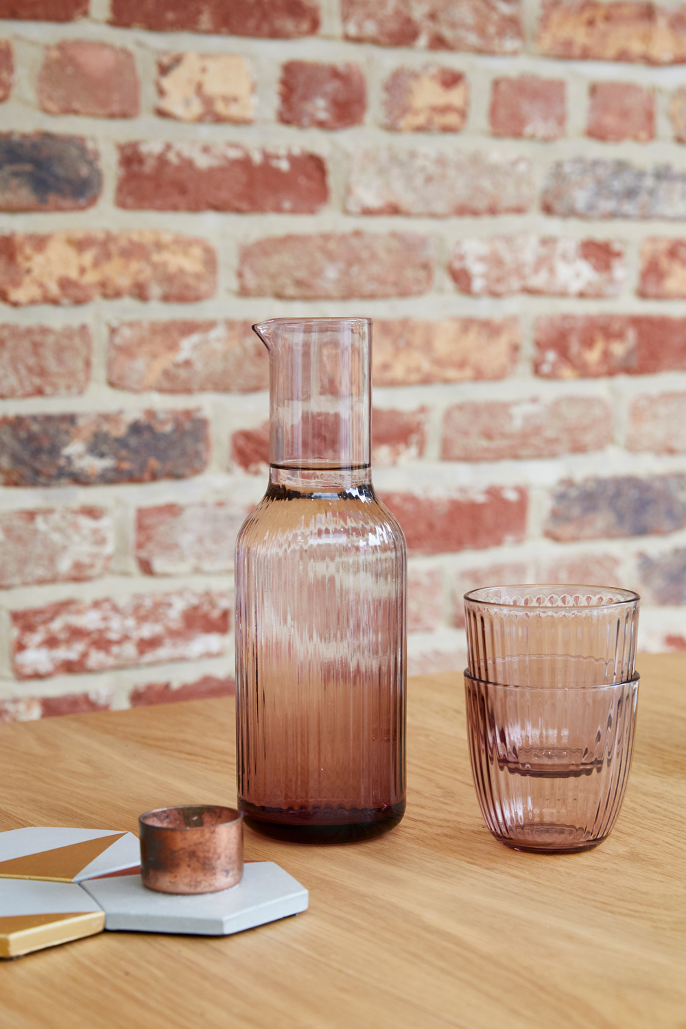 Pink glasses sit on oak dining table with exposed brick backdrop