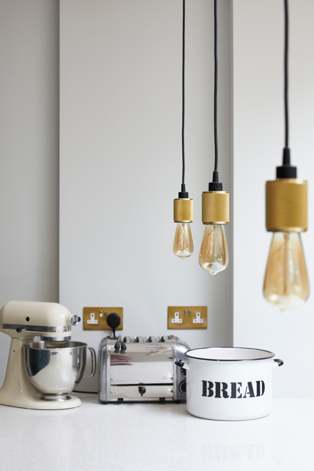 Toaster, Mixer and Bread post sit on white quartz worktop with heavy metal brass pendants by Buster and Punch hang above