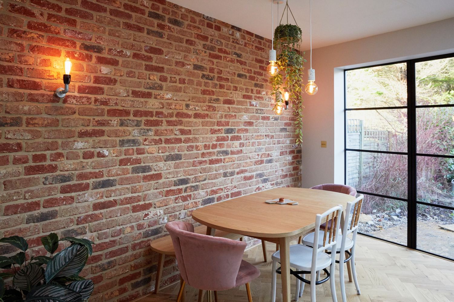 Exposed brick wall with clean oak dining table and upholstered chairs