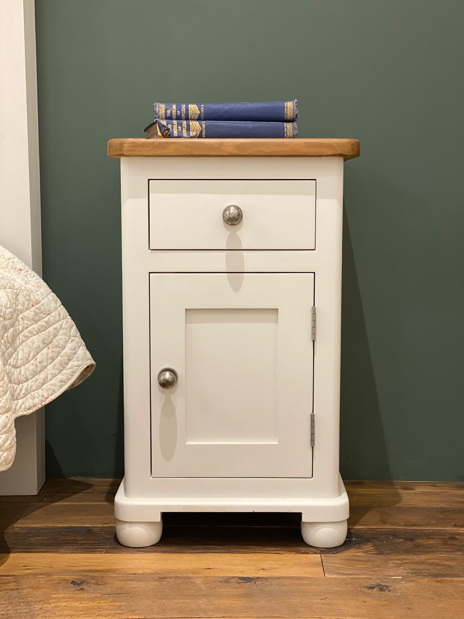 Painted round end bedside table with one door and one drawer against green wall