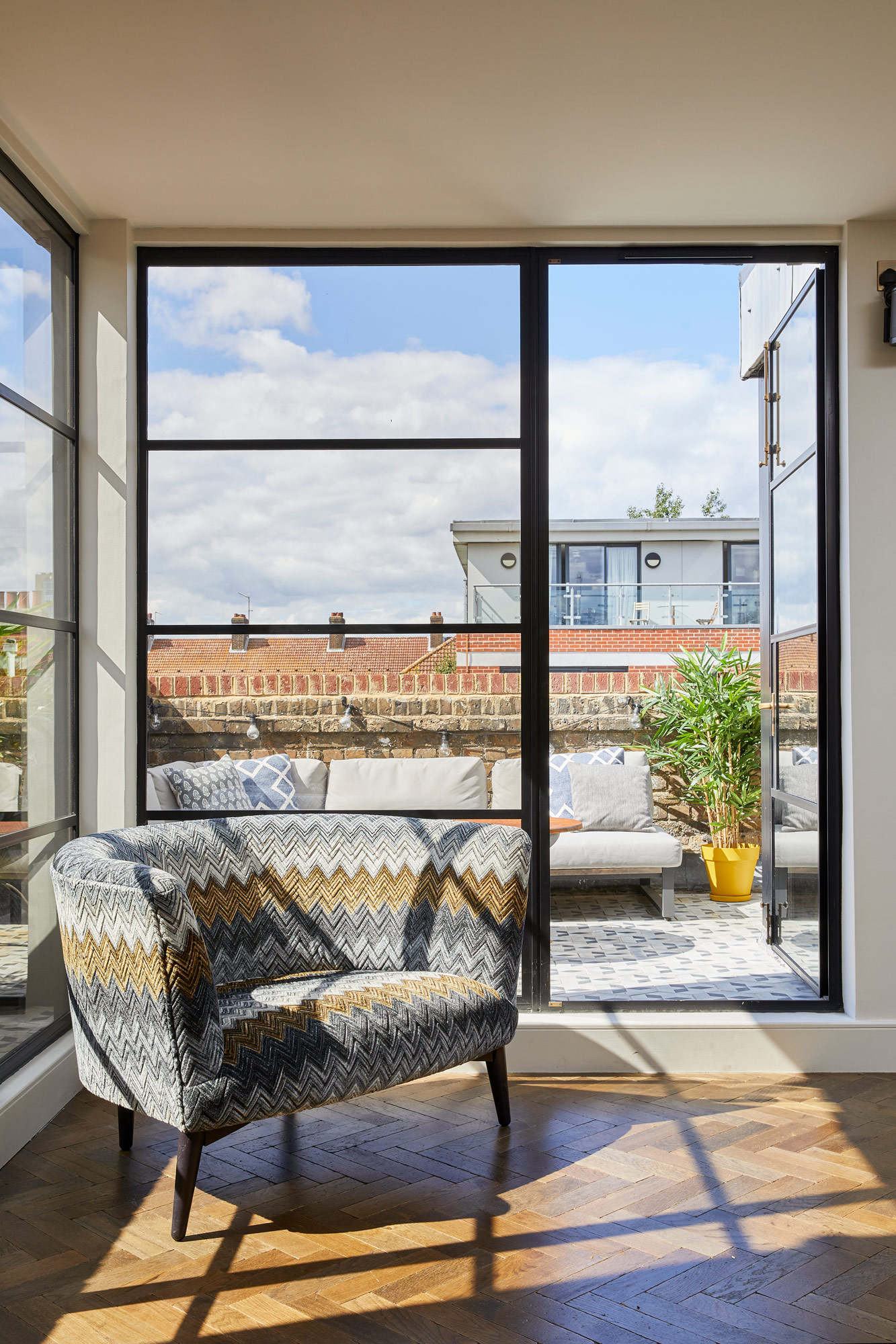 Sun shining through Crittall doors on to upholstered sofa and parquet flooring