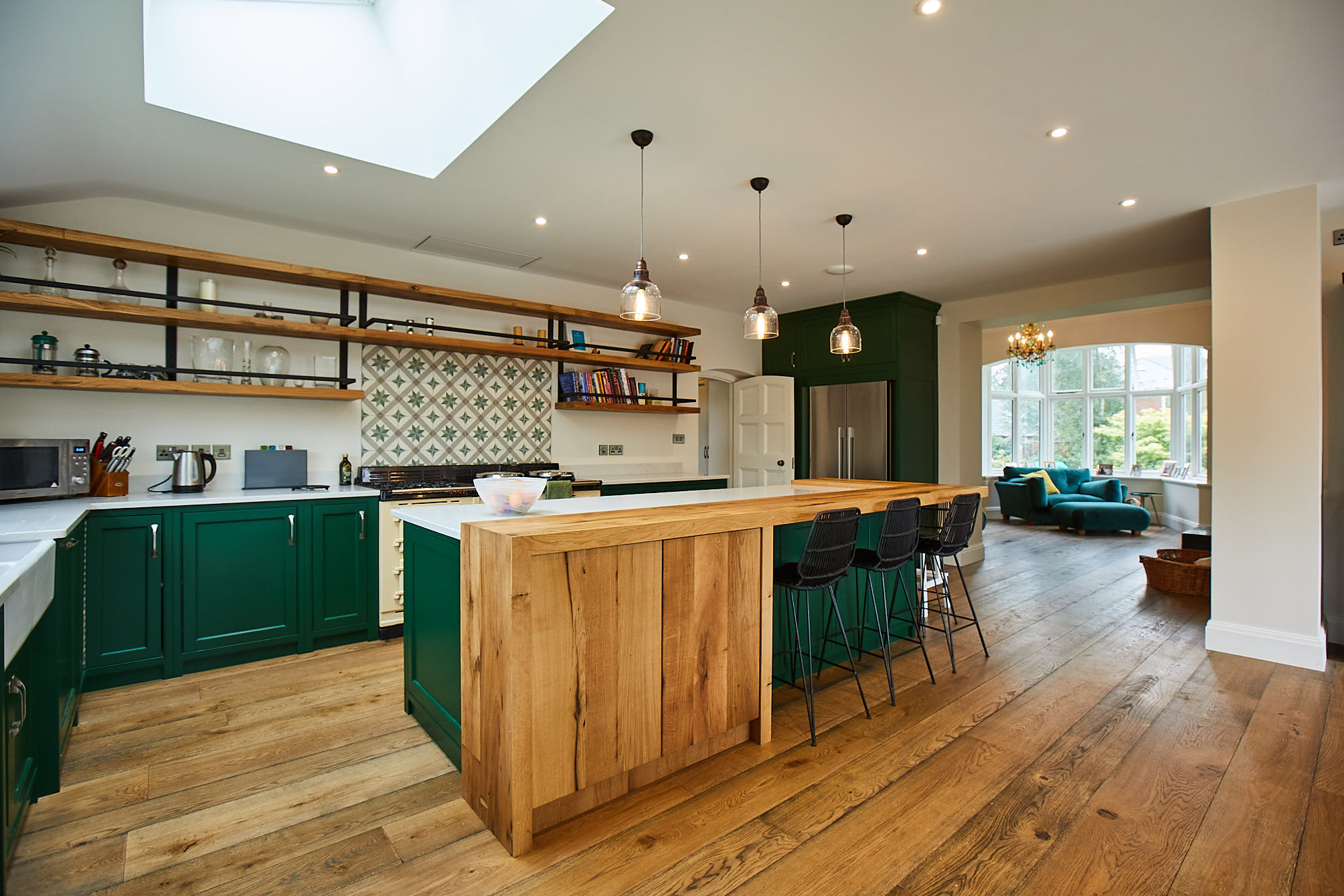 Large green kitchen with floating oak shelves and oak breakfast bar
