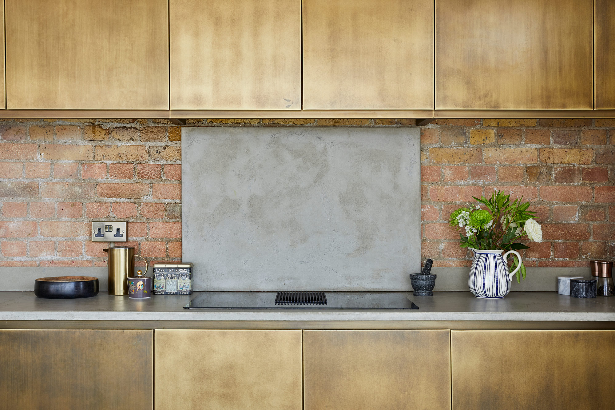Brass metal kitchen cabinets with concrete countertops and backsplash