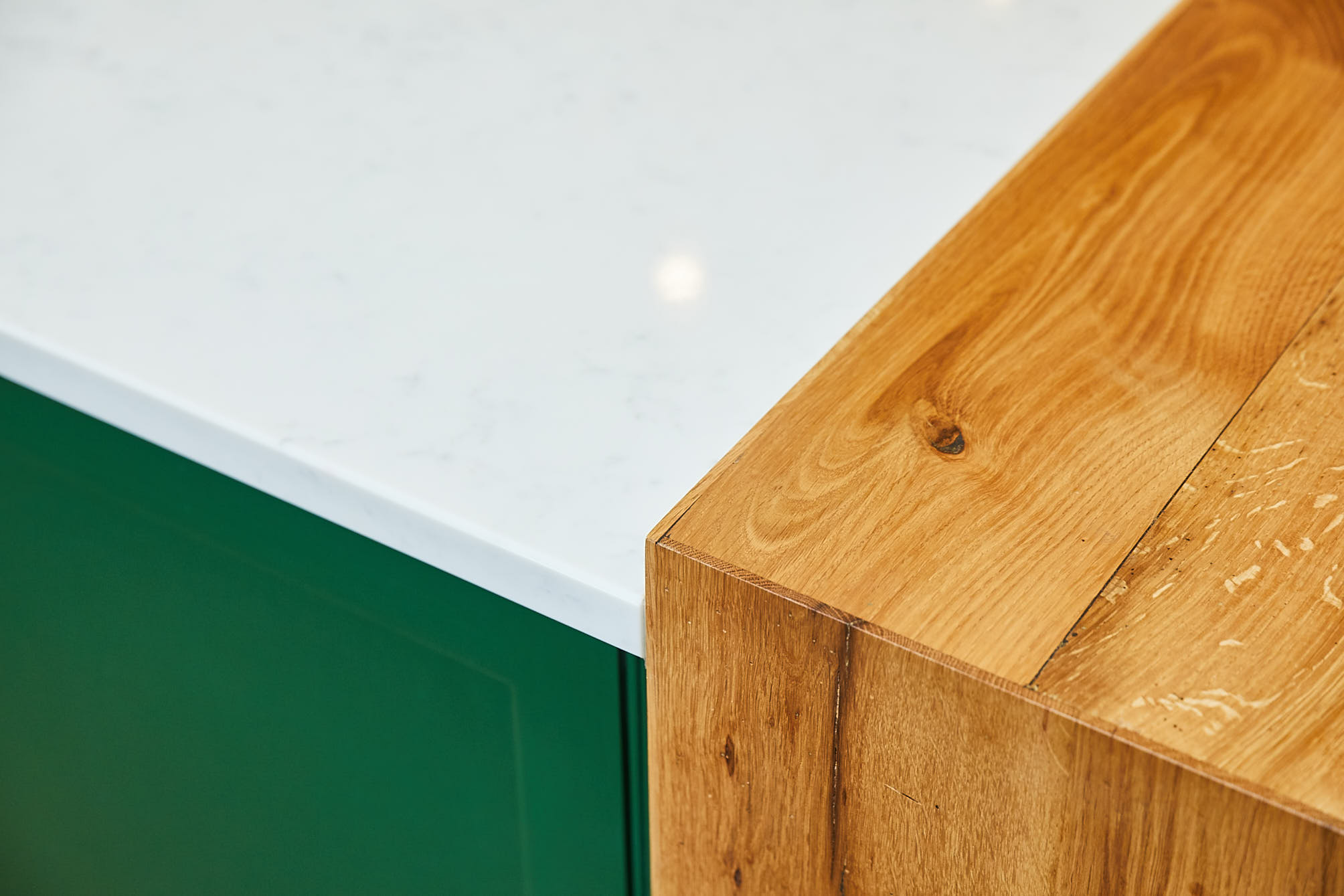 Oak breakfast bar against whitre quartz worktop and green painted kitchen cabinets