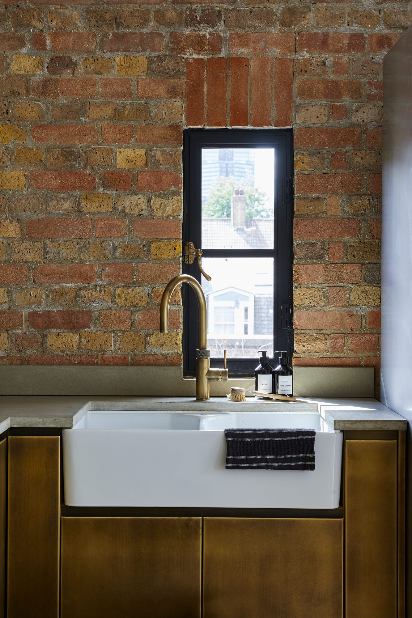 Ceramic belfast sink with concrete worktops and brass metal kitchen cabinets