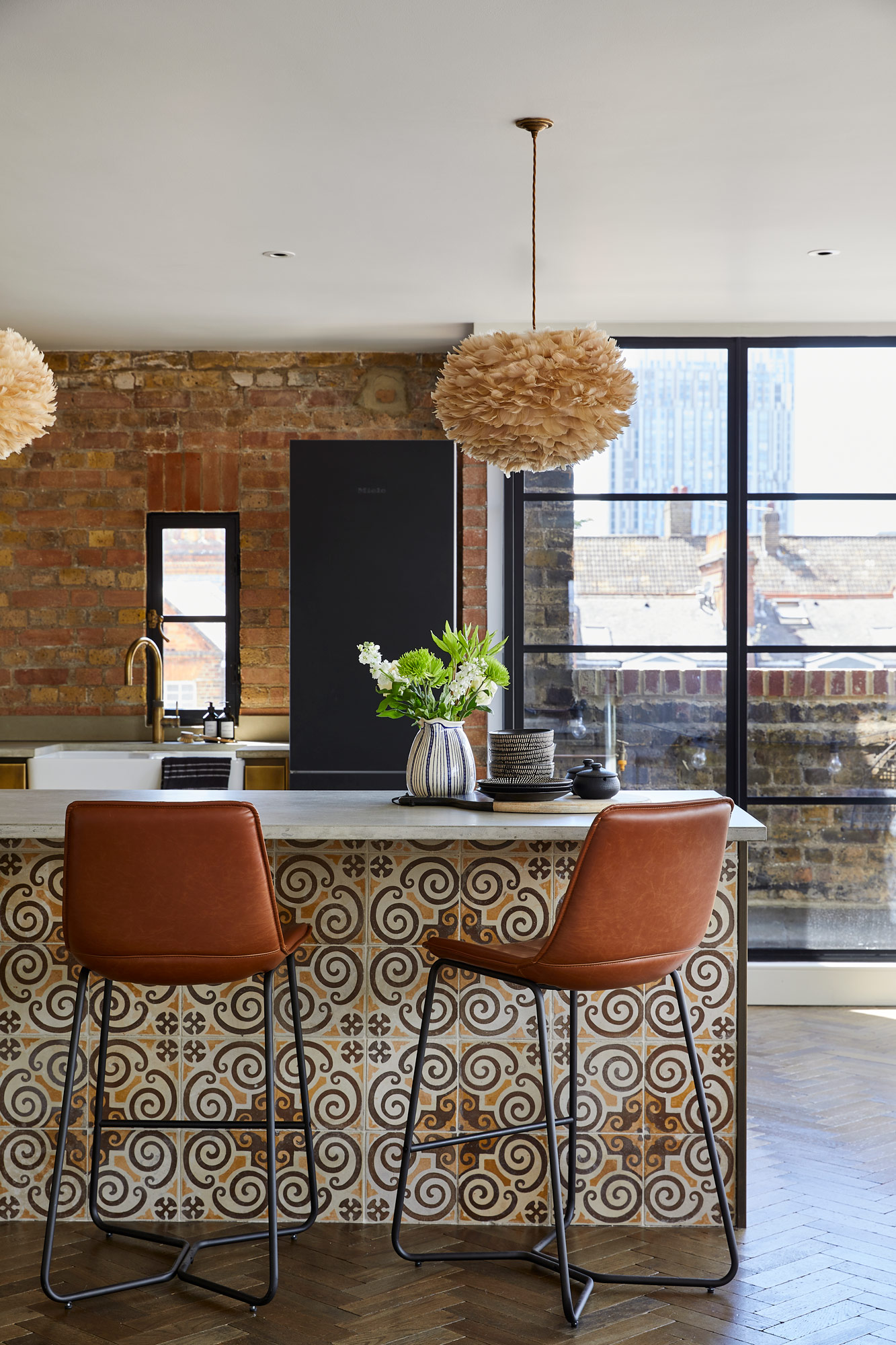 Brown leather barstools sit under metal kitchen with reclaimed tile kickboard