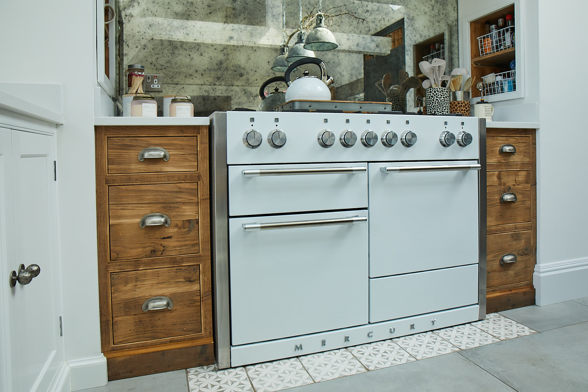 Rustic pan drawers beside white range cooker with antique mirror backsplash