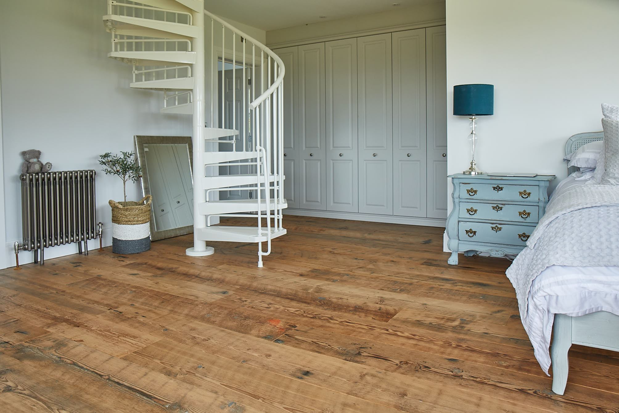 Rustic flooring contrasts with white fitted wardrobes and spiral staircase in bedroom