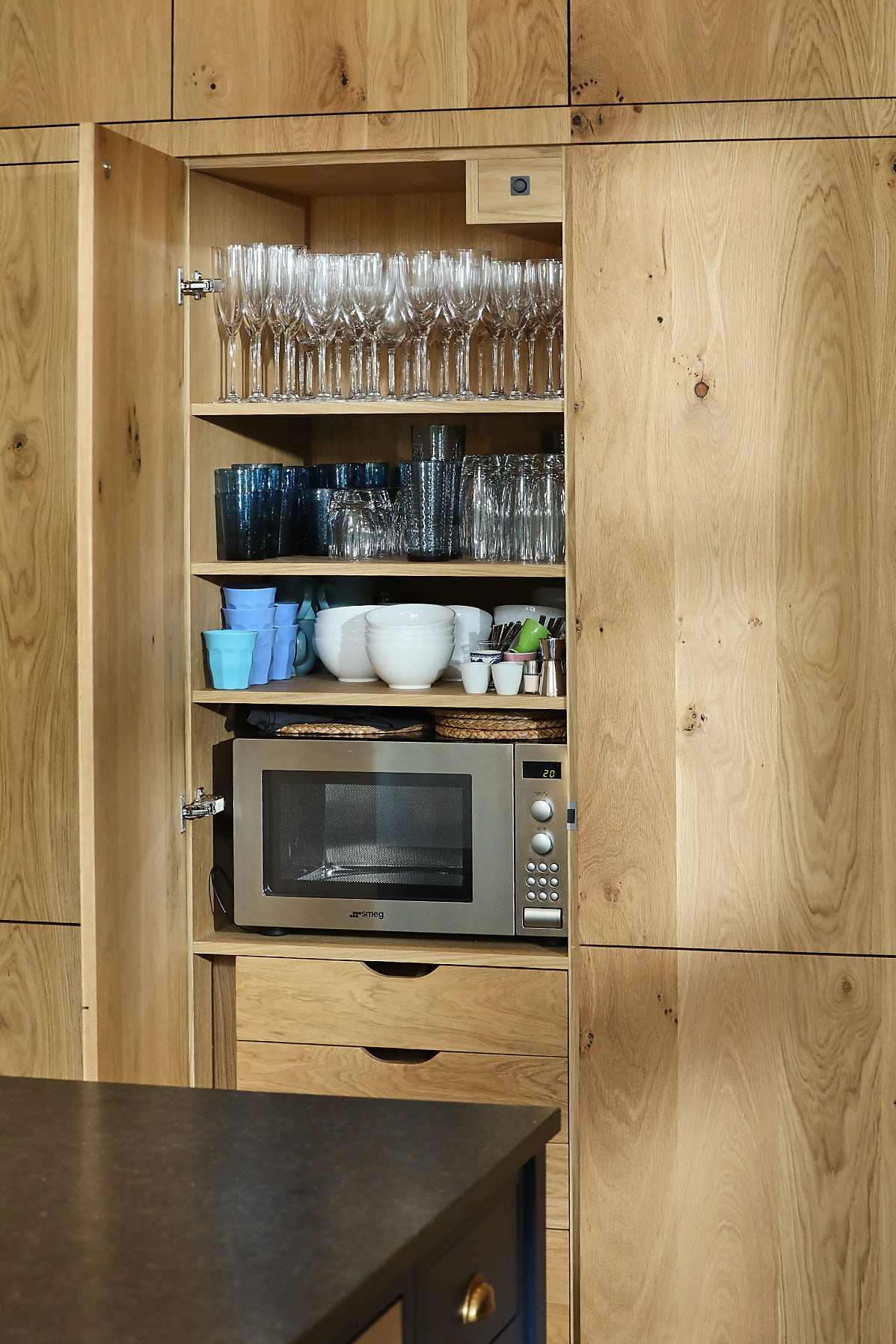 Glasses and microwave stored in tall oak kitchen cabinets