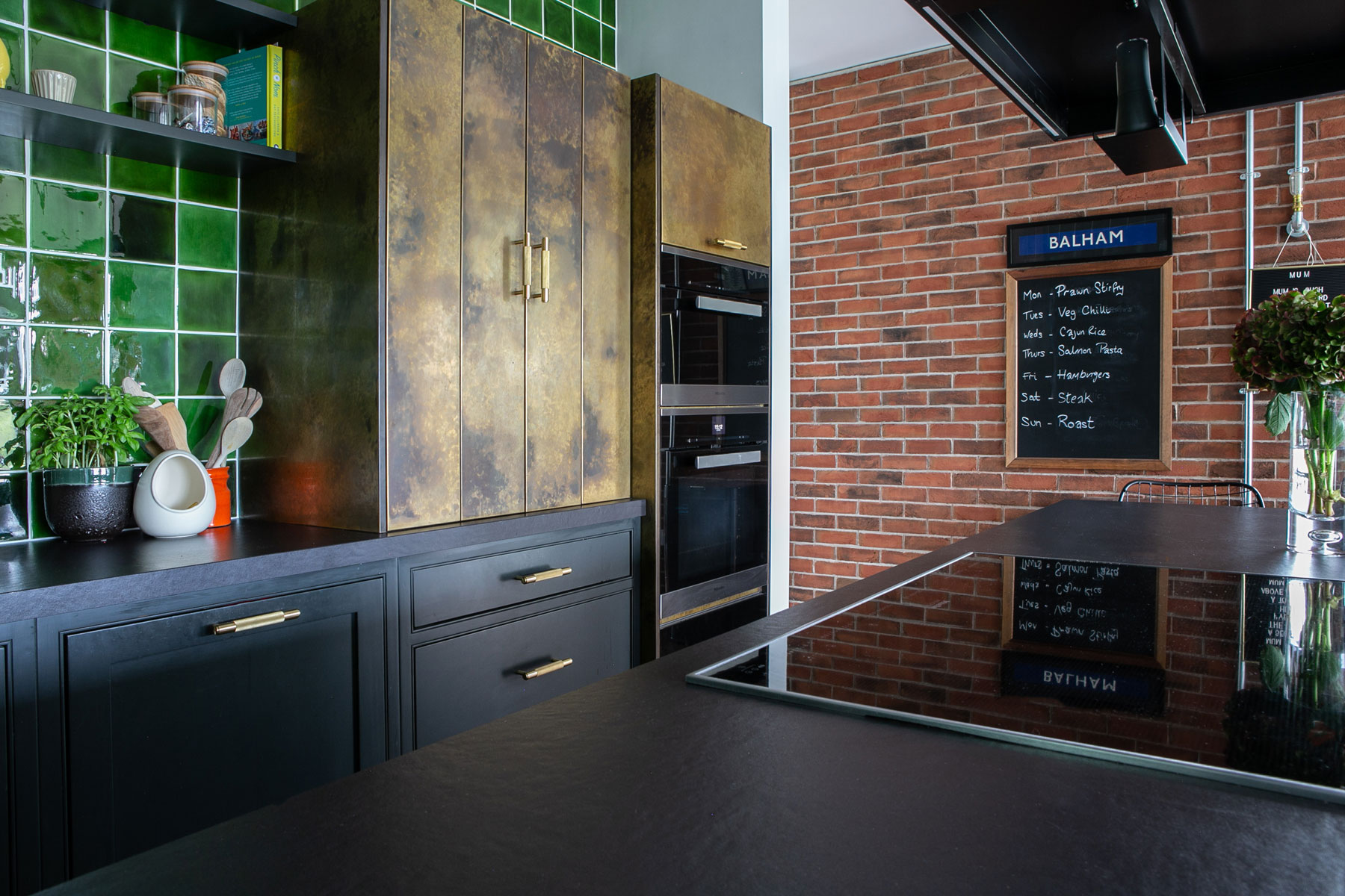 Aged brass bi fold kitchen cabinet with green porcelain tile backsplash